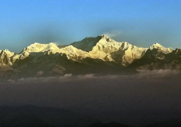 snow-capped Kanchenjunga mountain range illuminated in warm, golden hues during sunrise, seen from Tiger Hill as part of a Darjeeling Sightseeing Package Tour