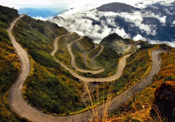Winding mountain road with iconic hairpin bends surrounded by clouds and mountains on the Zuluk Silk Route in East Sikkim.